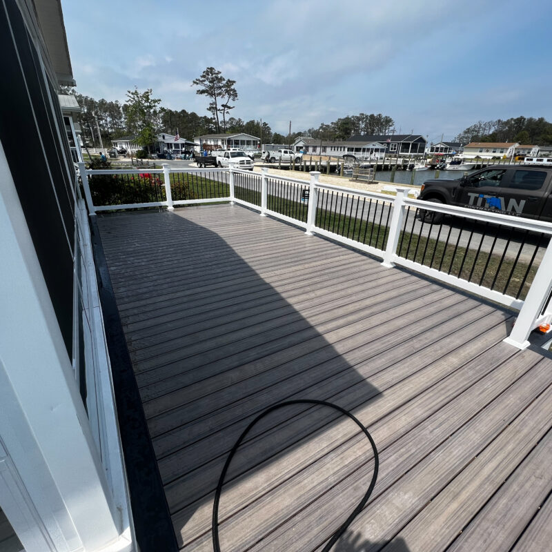 A completed waterfront deck featuring grey composite boards and white railing overlooking a lake and boat dock.