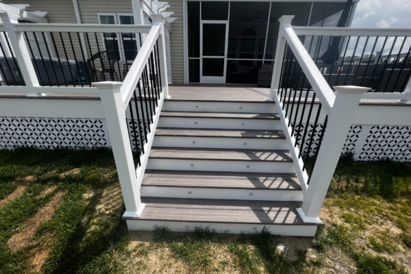 Modern deck staircase featuring grey composite treads, white PVC risers, and black metal balusters with white railing posts.
