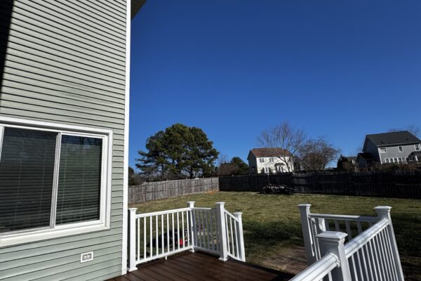 POV perspective of a custom Trex deck with white vinyl railings and brown composite boards in a Garner, NC residential backyard.