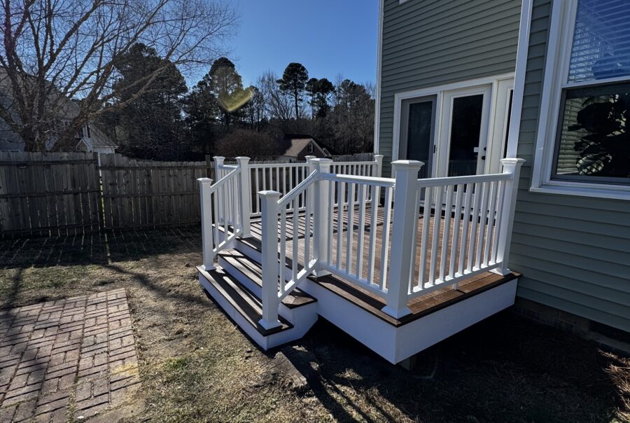 POV view of a custom Trex composite deck with white vinyl railings and stairs, leading to the back entrance of a home in Garner, NC