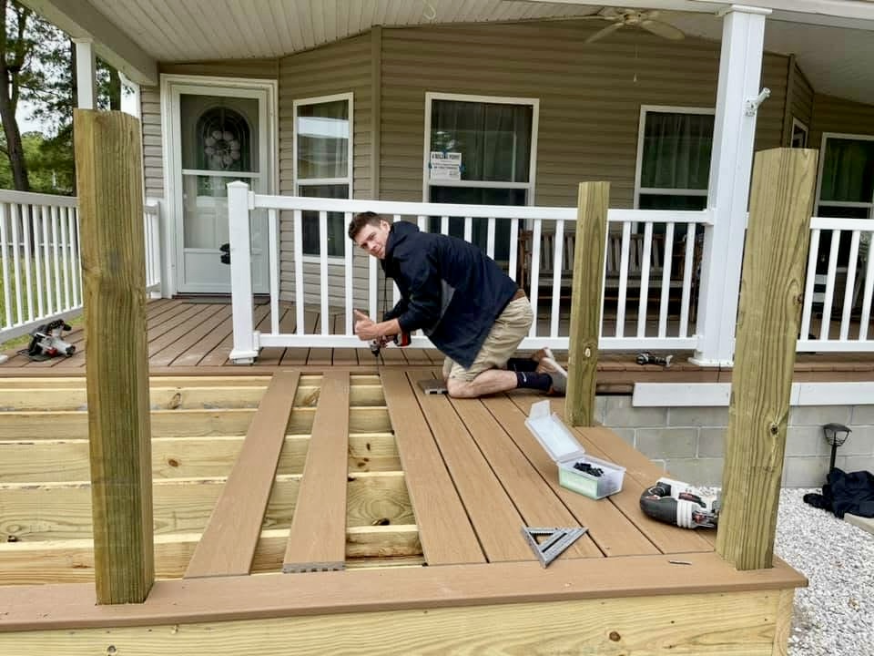 Kyle Speese, owner of Titan Decks, in a dark blue shirt pointing and installing composite deck boards on a residential project.