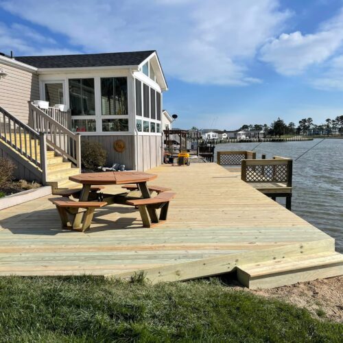 Completed-Wood-Deck-Waterfront-NC Completed wide wood deck and dock area with a picnic table on a North Carolina waterfront by Titan Decks.