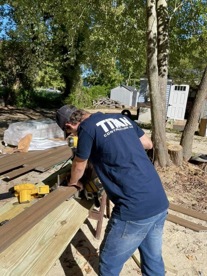 Kyle Speese, owner of Titan Decks, wearing a dark blue Titan Contracting LLC shirt while using a chop saw to cut deck boards.